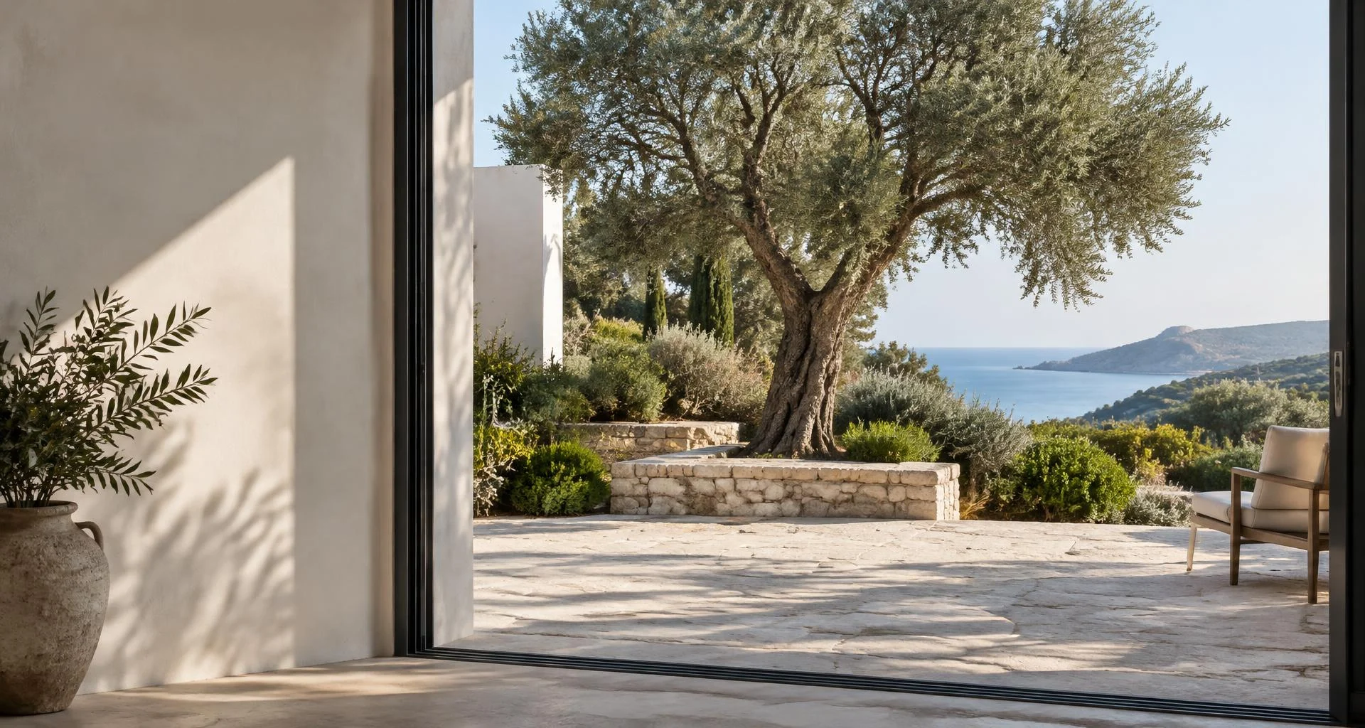 Una terraza abierta a un jardín de olivos y al mar, con luz natural